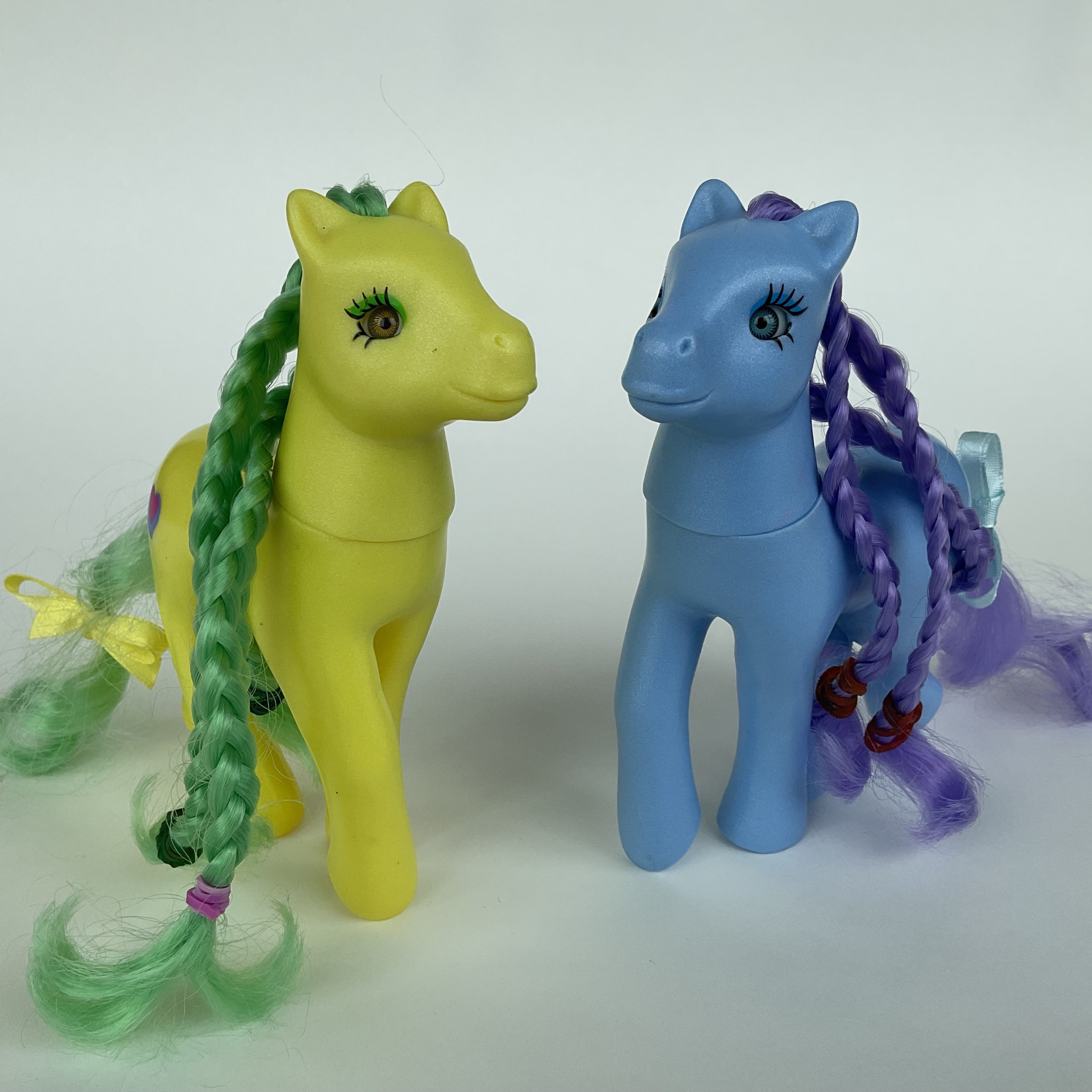 2 søde ponyfigurer med flettet hår – gul/grøn og blå/lilla – ca. 14 cm
