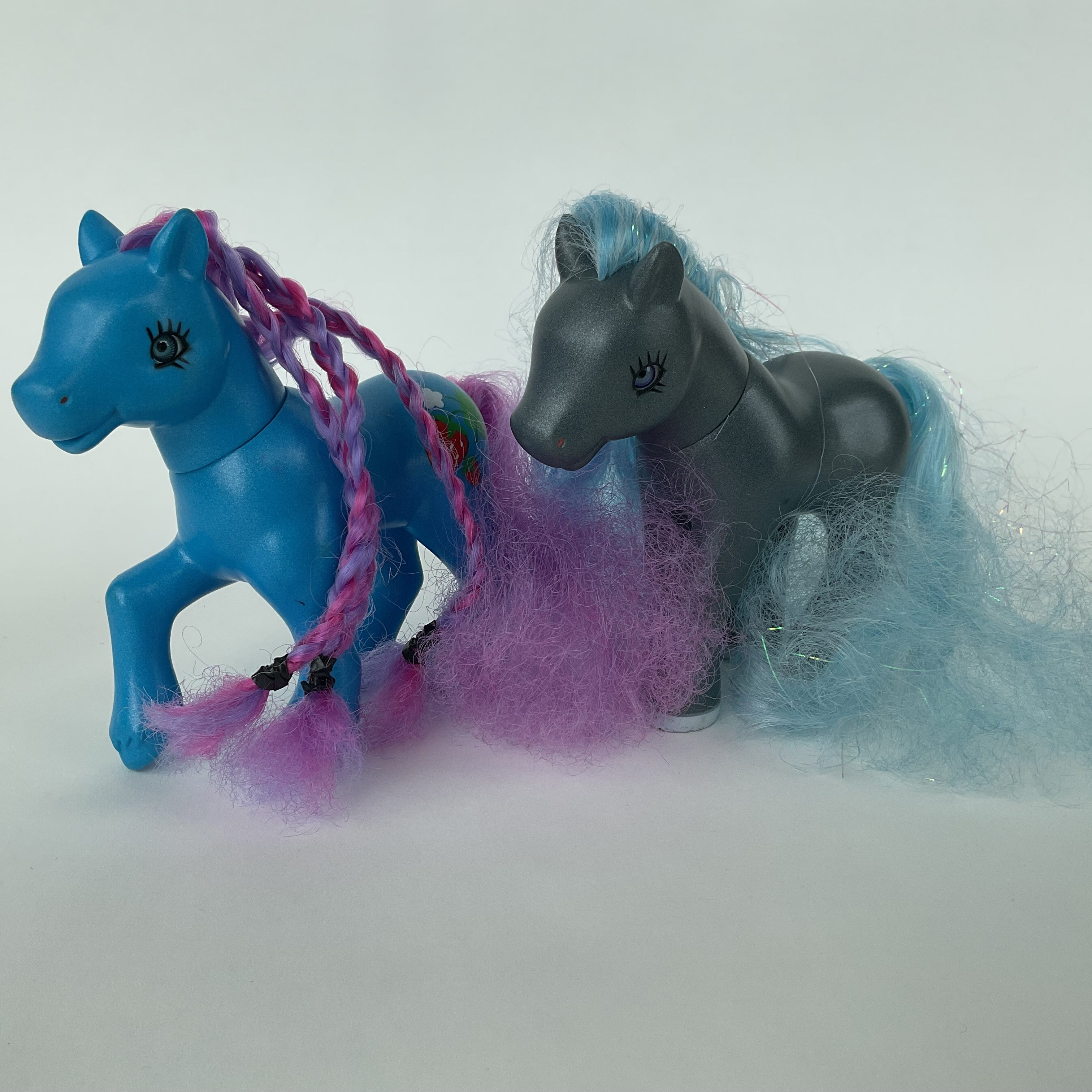 2 flotte ponyfigurer med farverigt hår – blå/lilla og grå/blå – ca. 14 cm